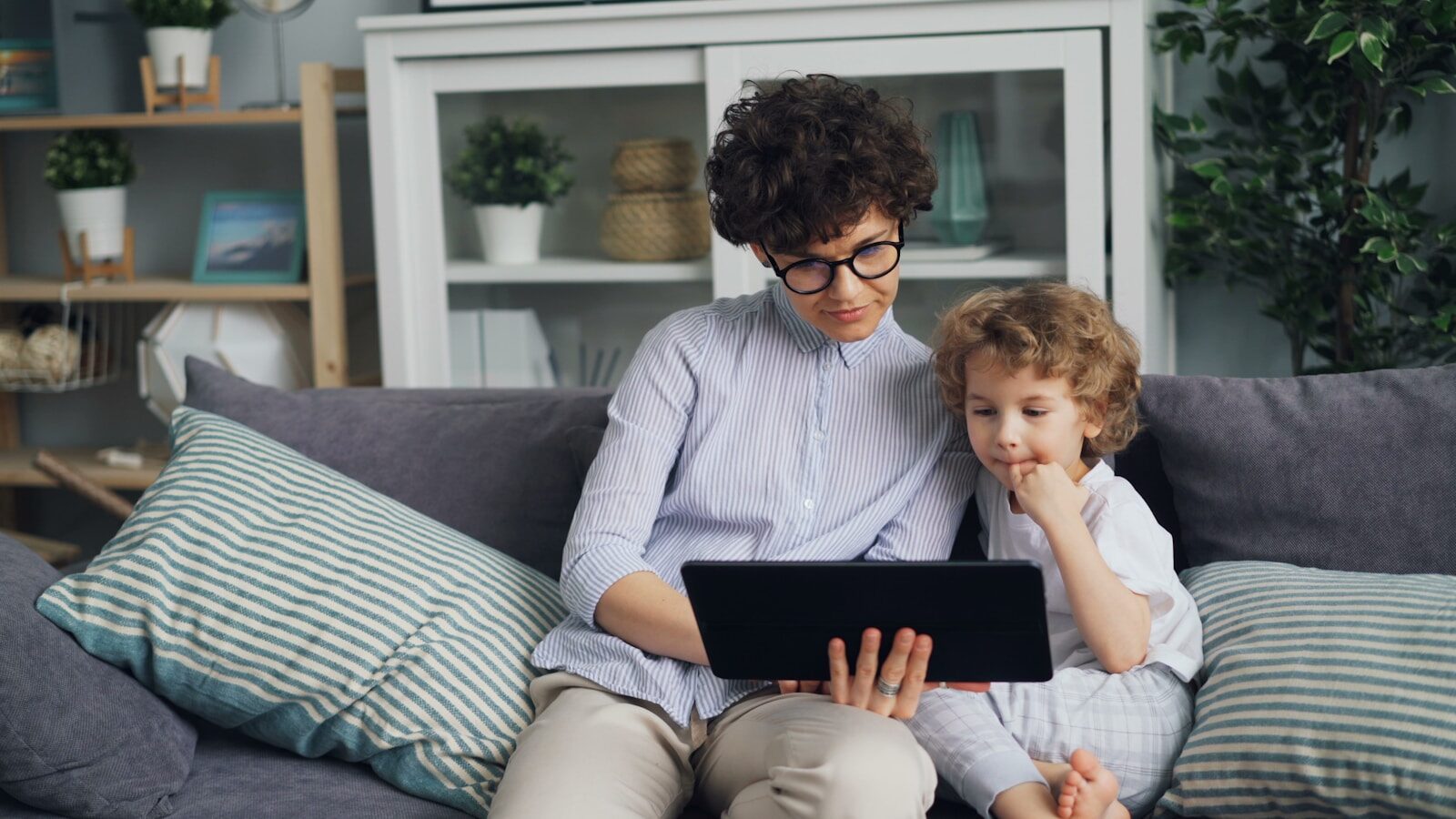 a woman and a child sitting on a couch looking at a laptop