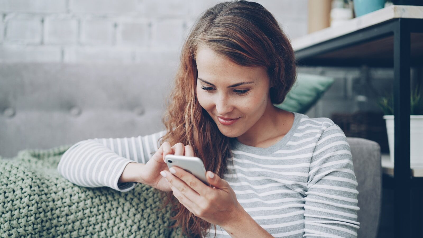 A young woman smiling while looking at her phone.